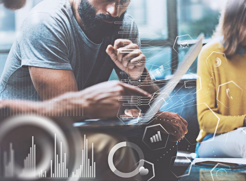 Two professionals, one with a doctorate, at a table with a laptop, surrounded by digital graphics of charts and data analysis overlays, illustrating a modern, tech-driven work environment.