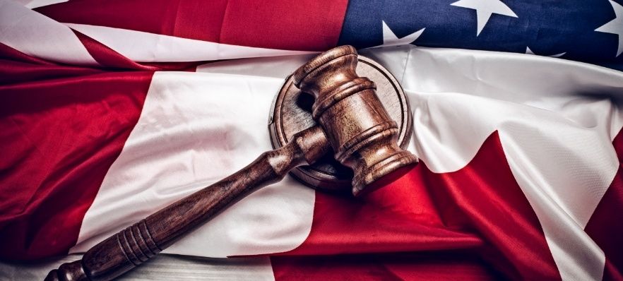 A wooden gavel resting on an American flag, symbolizing the intersection of law enforcement and patriotic values. The flag's stars and stripes are prominently displayed beneath the gavel.