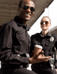 Two police officers, one smiling Black man and one smiling white woman, standing outside on a sunny day, with the man holding a coffee cup. This image aligns with discussions on career advancement within law enforcement agencies.