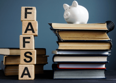 A white piggy bank sits on a stack of old books next to wooden blocks spelling "FAFSA" on a blue background, symbolizing financial aid for education.