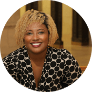 A woman with shoulder-length blonde hair and a warm smile, wearing a black and white polka dot blouse, seated indoors earning college credit.