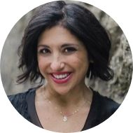 A smiling woman with dark hair and a black top, featuring a subtle necklace, set against a blurred natural background, perfectly embodies the essence of maximizing mental health.