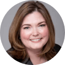 Professional headshot of a smiling college student with disabilities, featuring shoulder-length brown hair, dressed in professional attire and a light pink blouse, set against a blurred green background.