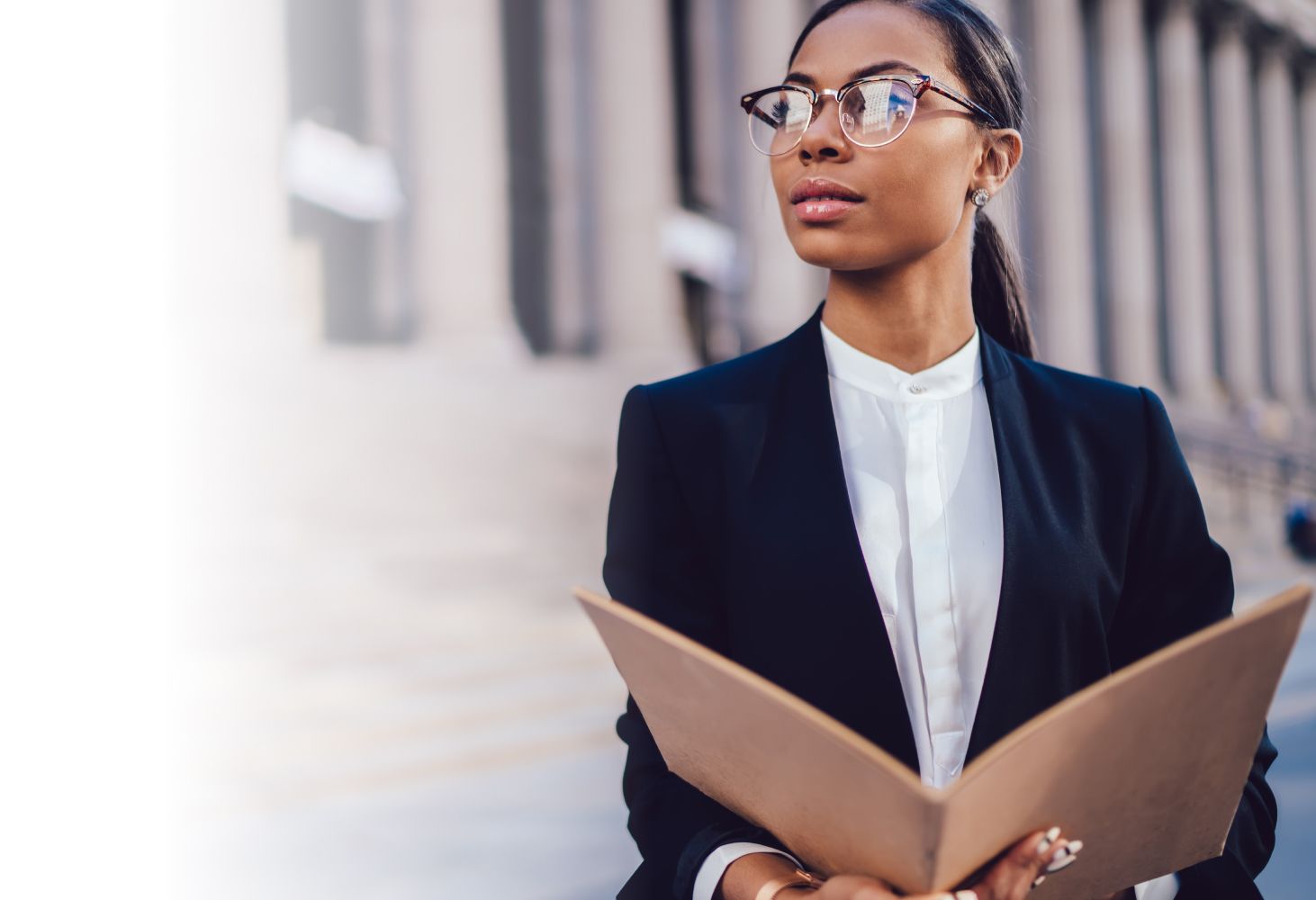 A professional paralegal in a black blazer and glasses holds an open folder, looking confidently to the side against a blurred city background.