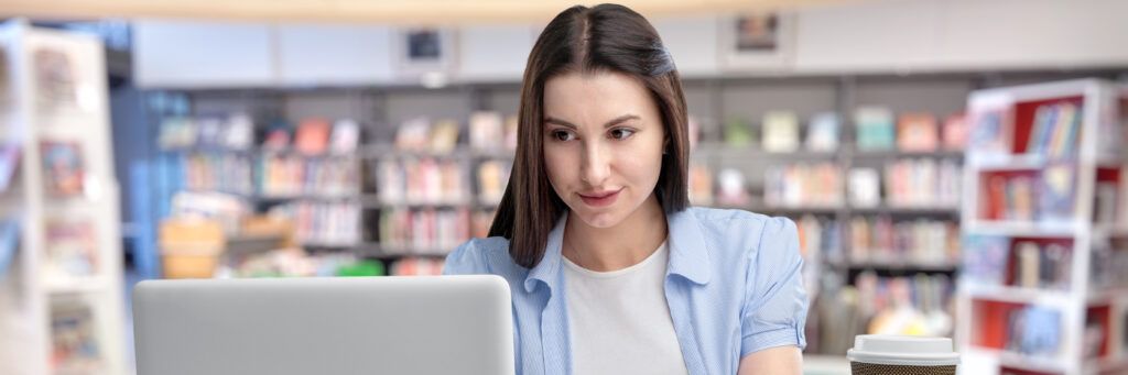 A female student sitting at a desk in the library looking at the laptop in front of her.