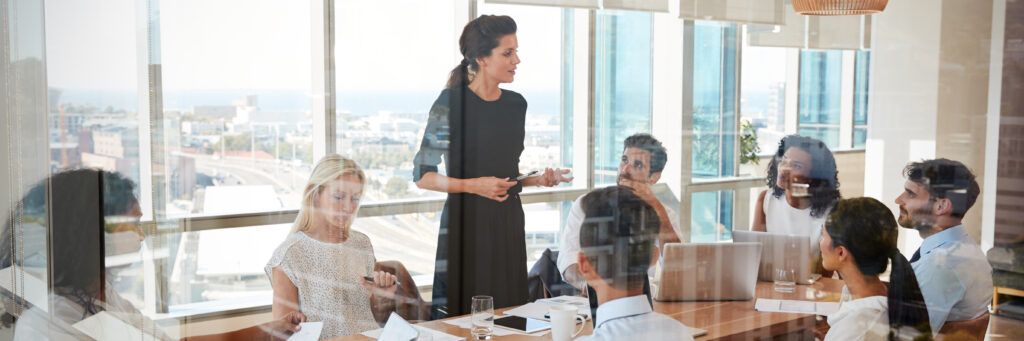 A woman in a black dress talking to colleagues in a public administration meeting.