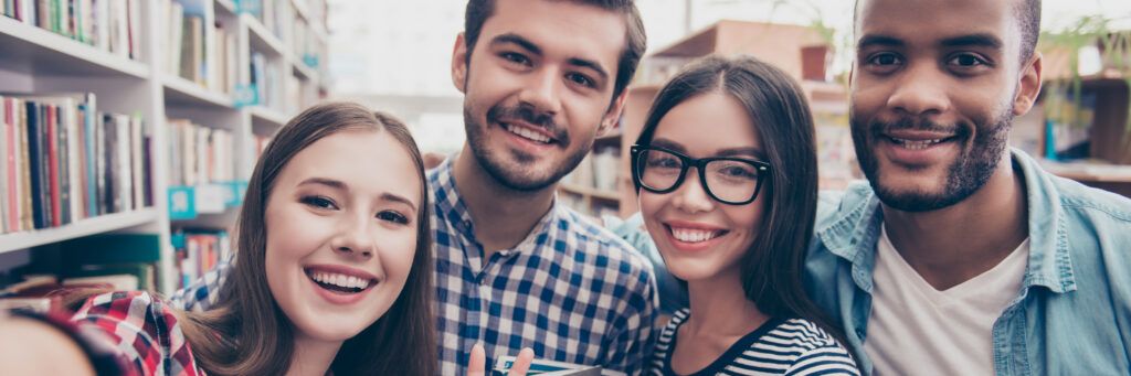Four smiling students stand together in the library.