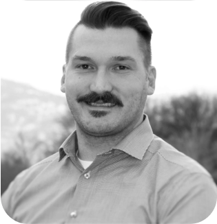 Black and white portrait of a smiling man with a styled mustache, wearing a collared shirt, standing outdoors with blurred nature in the background. It appears there is no specific content provided in the description you submitted regarding what the entity does or offers, only the phrase "About us." With only this